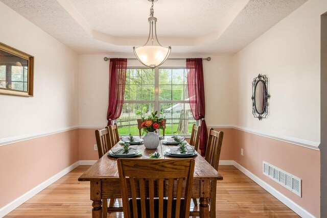 dining room with baseboards, a tray ceiling, light wood-style flooring, and visible vents