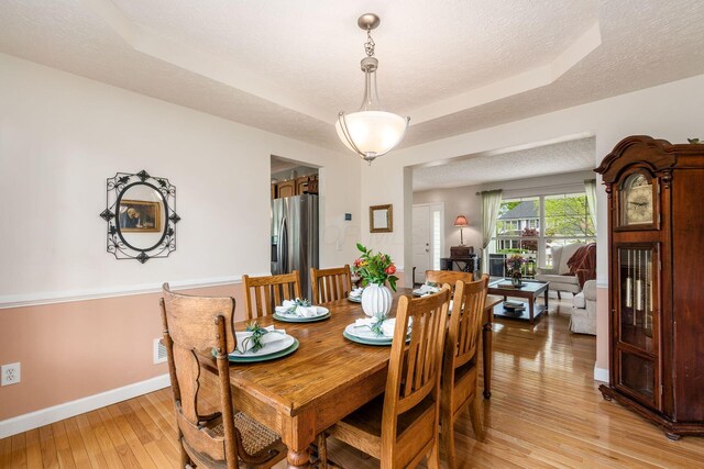 dining area with baseboards, a textured ceiling, light wood-style flooring, and a raised ceiling