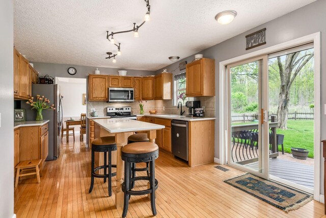 kitchen featuring backsplash, a center island, light wood-type flooring, light countertops, and stainless steel appliances
