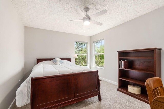 bedroom with a textured ceiling, baseboards, light carpet, and a ceiling fan