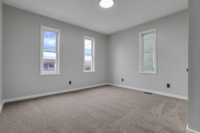 empty room featuring visible vents, carpet flooring, and baseboards
