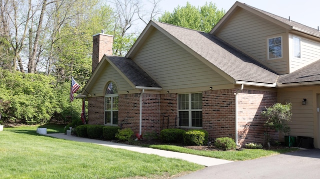 view of home's exterior featuring brick siding, roof with shingles, a yard, and a chimney
