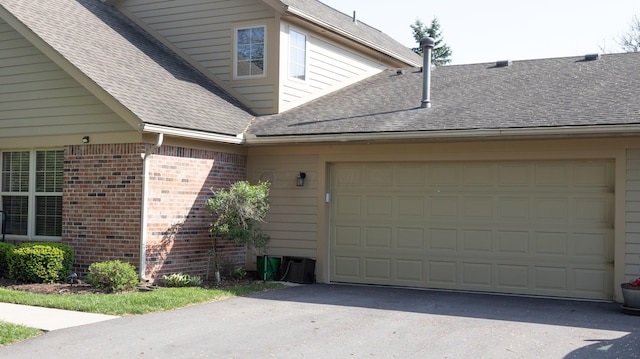 view of property exterior featuring brick siding, a shingled roof, an attached garage, and driveway