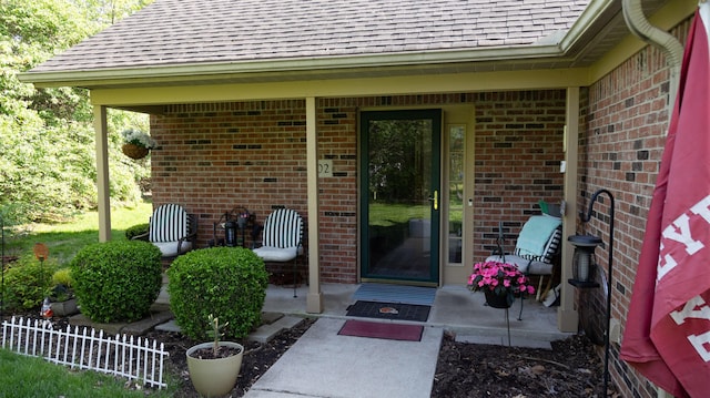 doorway to property with brick siding, a shingled roof, and a patio