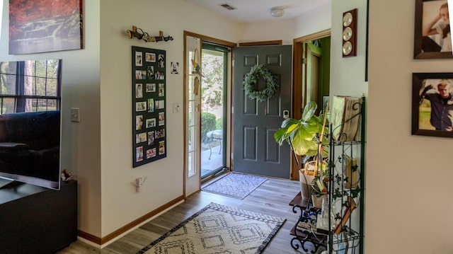 foyer entrance with baseboards, wood finished floors, and visible vents