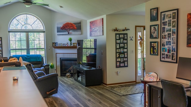living area featuring lofted ceiling, wood finished floors, baseboards, a tiled fireplace, and a ceiling fan