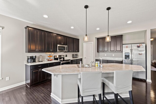 kitchen featuring dark brown cabinetry, baseboards, a kitchen bar, a sink, and stainless steel appliances