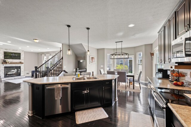 kitchen featuring a stone fireplace, dark wood-type flooring, light countertops, a sink, and appliances with stainless steel finishes