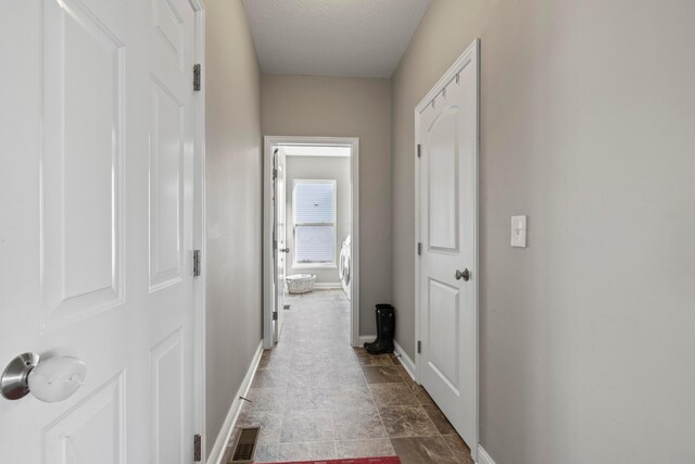 corridor featuring stone finish flooring, baseboards, and visible vents