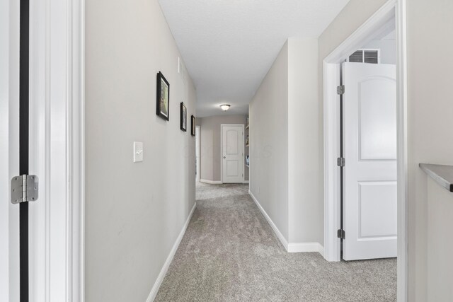 hall featuring baseboards, visible vents, and light carpet