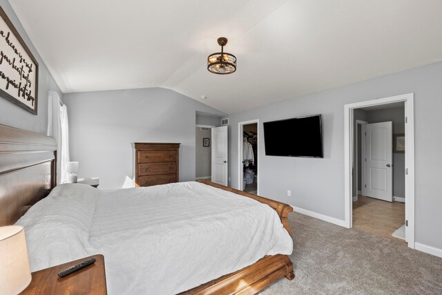 bedroom featuring carpet flooring, a walk in closet, visible vents, baseboards, and vaulted ceiling