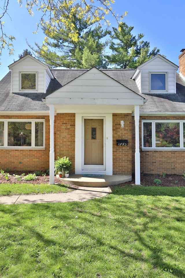 new england style home with brick siding, a shingled roof, and a front yard