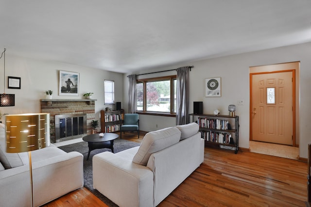 living room with a brick fireplace, baseboards, and wood finished floors