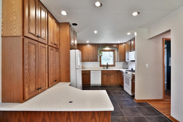 kitchen featuring dark tile patterned floors, brown cabinets, a sink, recessed lighting, and white appliances