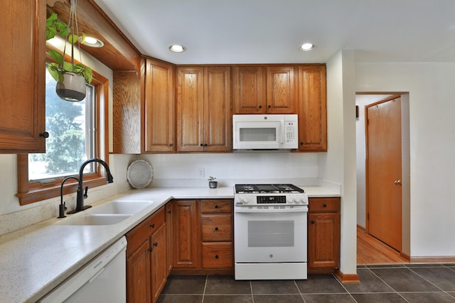 kitchen with white appliances, light countertops, brown cabinets, dark tile patterned flooring, and a sink