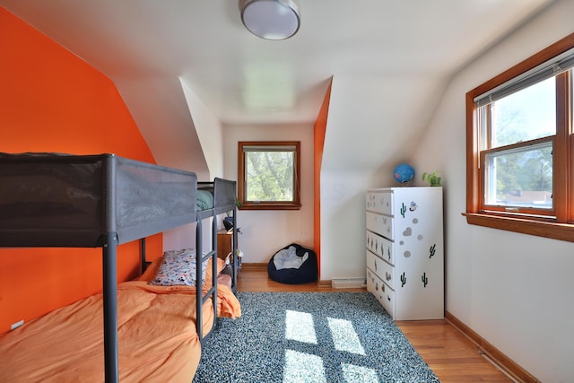 bedroom featuring baseboards, wood finished floors, and lofted ceiling