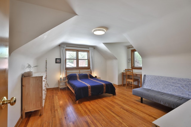 bedroom featuring baseboards, vaulted ceiling, multiple windows, and light wood-style flooring