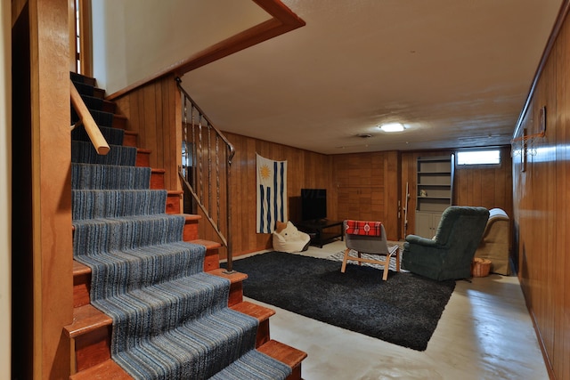 living room featuring wooden walls, stairway, and concrete flooring