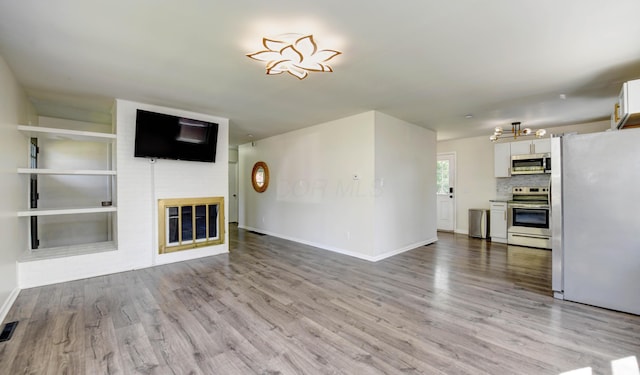 4589 Annhurst Rd, Columbus, OH 43228 - unfurnished living room featuring light wood-style flooring, baseboards, a glass covered fireplace, and a chandelier