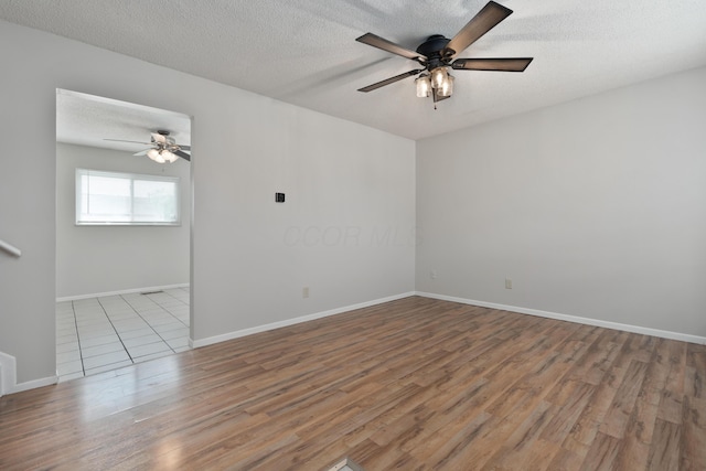 empty room with ceiling fan, wood finished floors, a textured ceiling, and baseboards