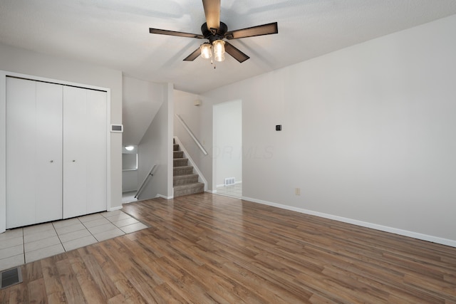 unfurnished living room with wood finished floors, a ceiling fan, baseboards, and stairs