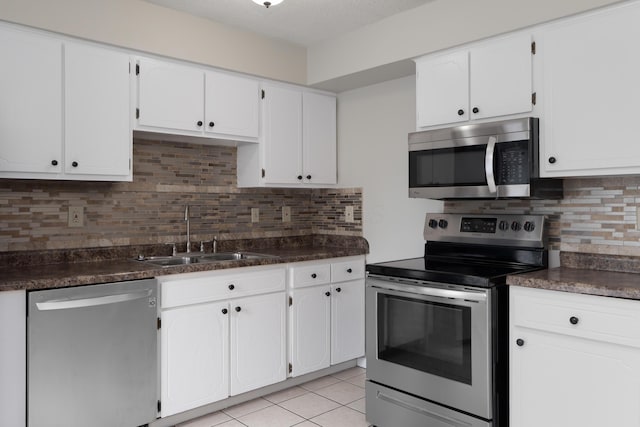 kitchen featuring stainless steel appliances, a sink, decorative backsplash, dark countertops, and white cabinetry