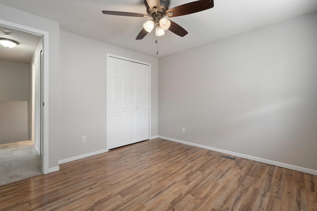 unfurnished bedroom featuring wood finished floors, baseboards, a closet, a ceiling fan, and a textured ceiling