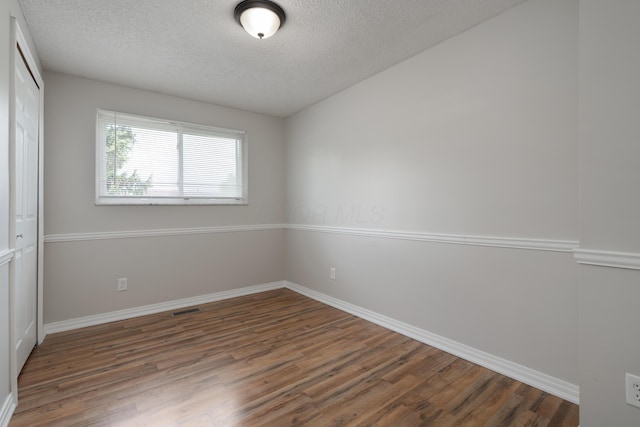 spare room featuring wood finished floors, a textured ceiling, and baseboards