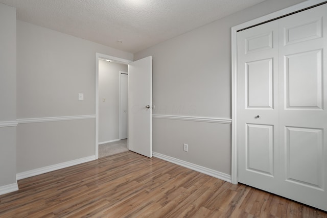 unfurnished bedroom featuring wood finished floors, a textured ceiling, baseboards, and a closet