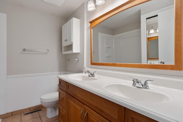full bath featuring wainscoting, tile patterned floors, toilet, and double vanity