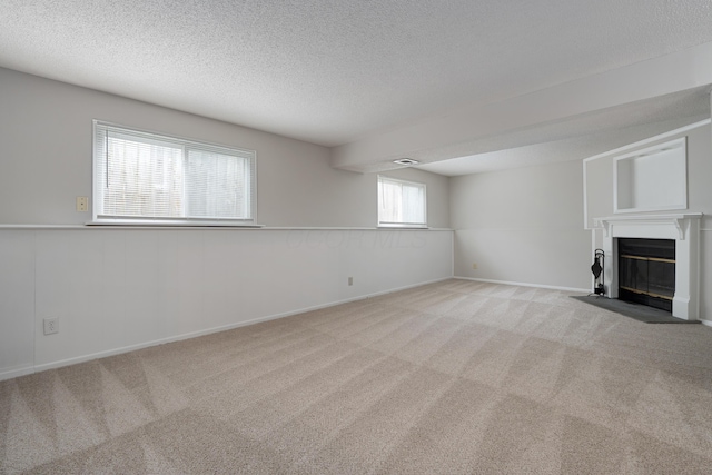unfurnished living room with carpet floors, a textured ceiling, a fireplace with flush hearth, and baseboards