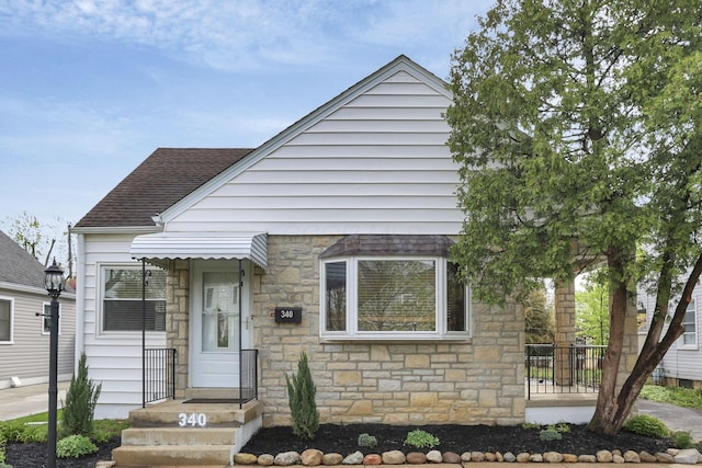view of front of property with roof with shingles, fence, and stone siding