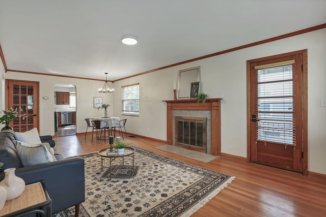 living area with crown molding, wood finished floors, a fireplace, baseboards, and arched walkways