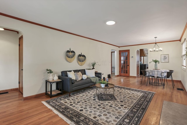 living area with crown molding, arched walkways, a chandelier, hardwood / wood-style floors, and baseboards