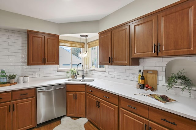 kitchen with stainless steel dishwasher, brown cabinetry, a sink, and light countertops