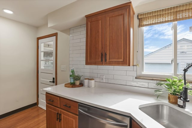 kitchen featuring stainless steel dishwasher, decorative backsplash, brown cabinetry, light countertops, and light wood-style flooring