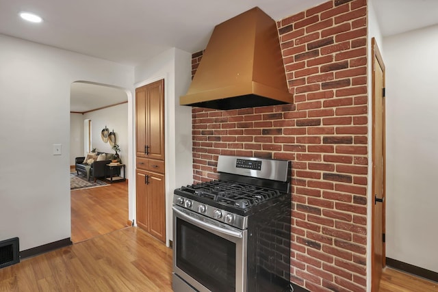 kitchen with light wood finished floors, arched walkways, wall chimney exhaust hood, gas range, and visible vents