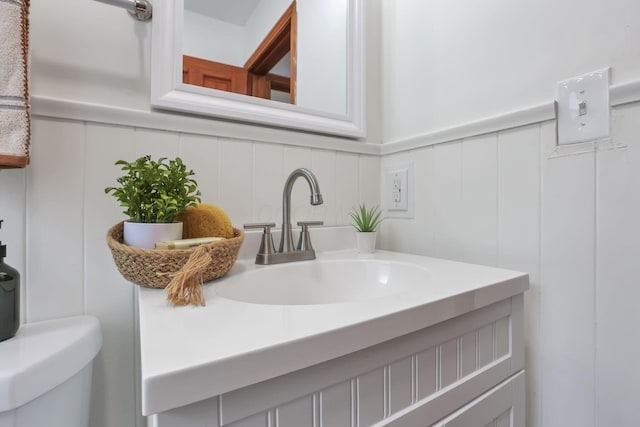 half bath featuring vanity, a decorative wall, and toilet