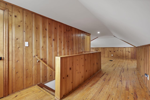 additional living space featuring wood walls, vaulted ceiling, and light wood-style floors