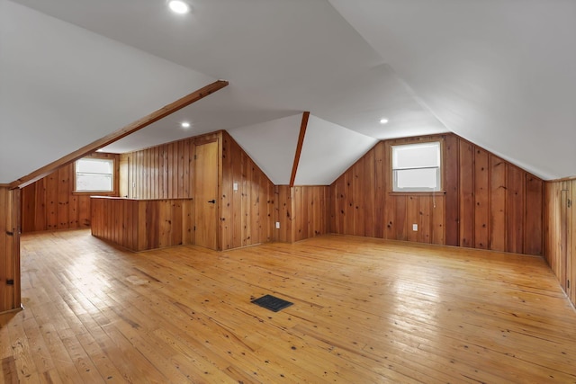 bonus room with wooden walls, vaulted ceiling, light wood-style flooring, and visible vents