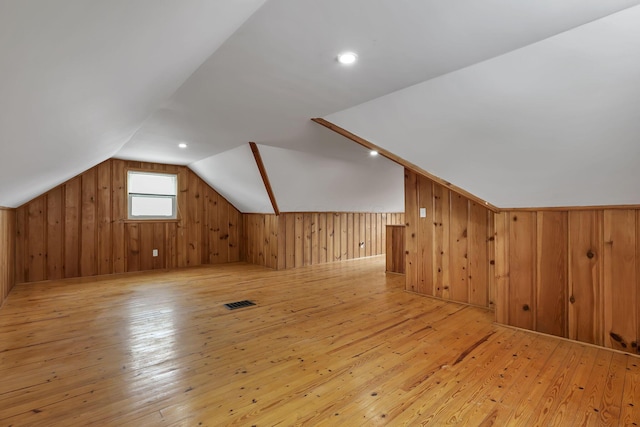 bonus room featuring visible vents, wood walls, light wood-style flooring, and vaulted ceiling