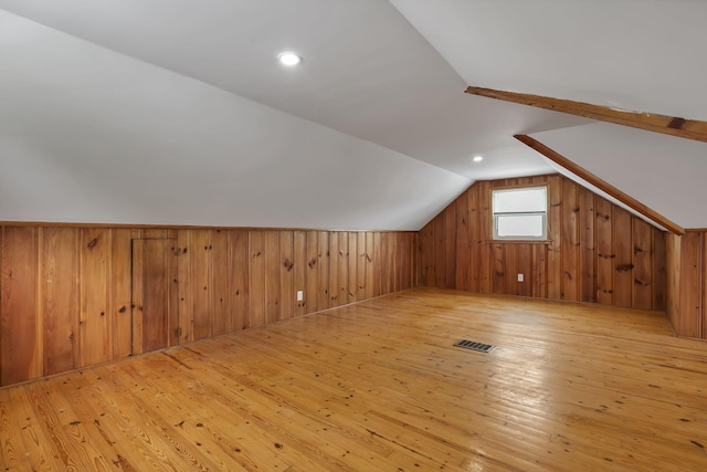 bonus room featuring wood walls, visible vents, light wood finished floors, and lofted ceiling