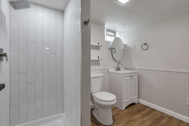 full bath with vanity, wood finished floors, toilet, tiled shower, and a wainscoted wall