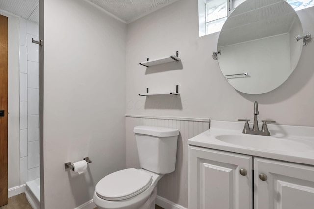 bathroom featuring vanity, baseboards, toilet, and tiled shower