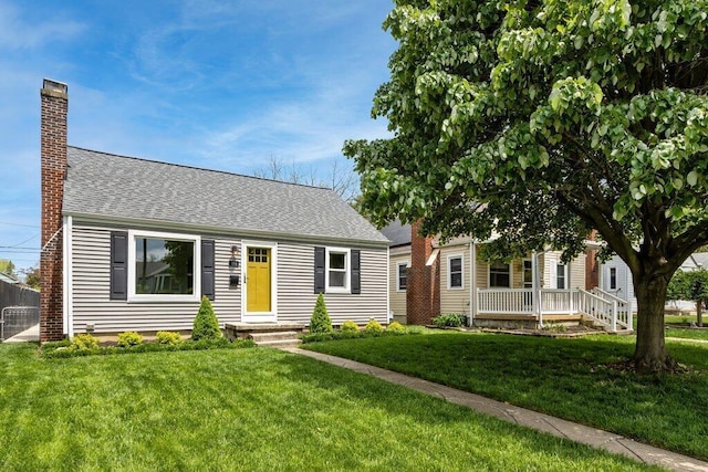 view of front of property with a chimney, a front yard, and roof with shingles