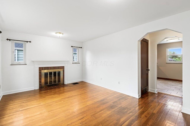 unfurnished living room with hardwood / wood-style floors, visible vents, a brick fireplace, arched walkways, and baseboards