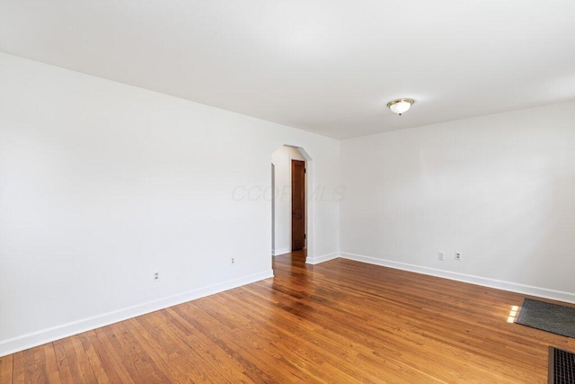 unfurnished room featuring arched walkways, baseboards, visible vents, and wood finished floors