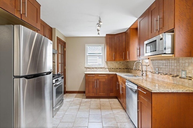 kitchen with light stone countertops, a sink, brown cabinets, tasteful backsplash, and appliances with stainless steel finishes
