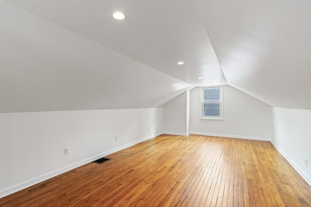 additional living space featuring light wood-type flooring, lofted ceiling, visible vents, and baseboards