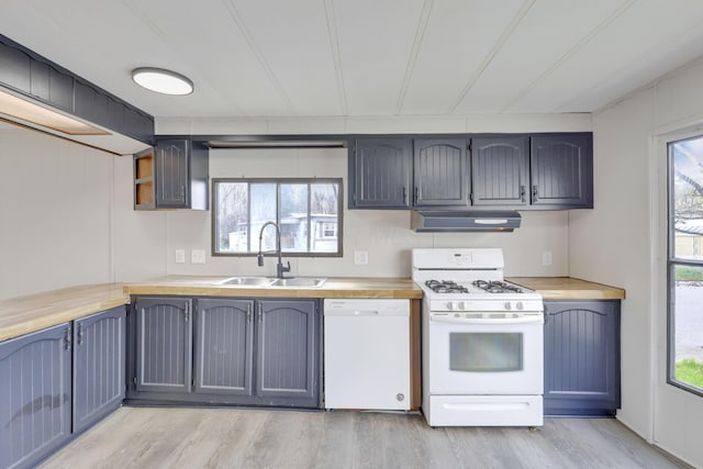 kitchen with white appliances, light wood-type flooring, light countertops, under cabinet range hood, and a sink